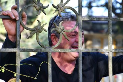 Close-up of happy mature man looking away while standing by metal fence