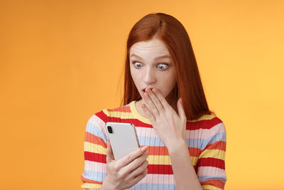 Portrait of young woman using smart phone against orange background