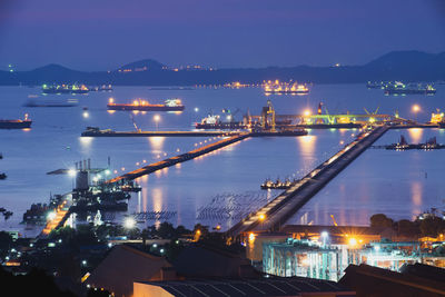 Illuminated city by sea against sky at night