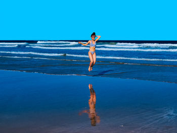 Happy young woman with a beautiful body living a healthy lifestyle jumping waves on beach shore