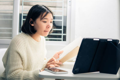 Young woman using phone while sitting on table