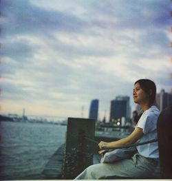 Side view of young man looking at sea against sky