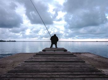 Rear view of man fishing on pier against sky