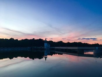 Silhouette man standing by lake against sky during sunset