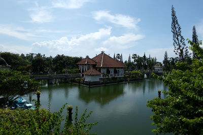 House by lake and buildings against sky