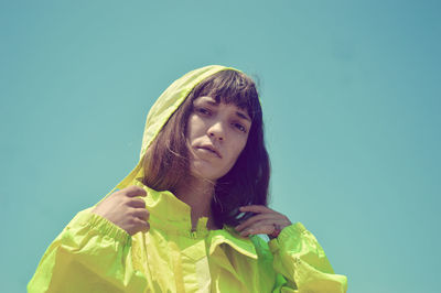 Low angle view of young woman holding gift against clear blue sky