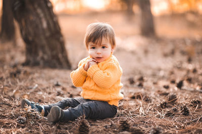 Cute boy sitting in forest by trees