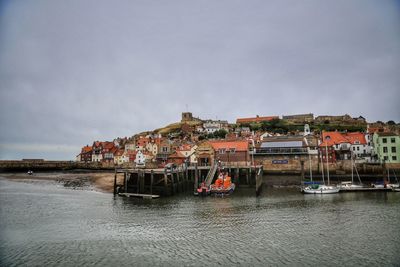 Sailboats in sea by houses against sky in city