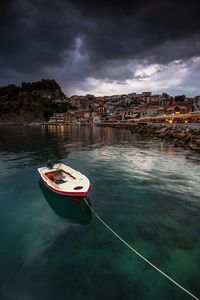 Boat moored on sea by town against sky