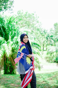 Portrait of young woman standing against trees