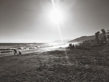 Silhouette people walking on beach against sky