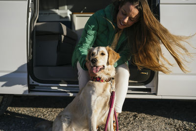 Mid adult woman stroking dog sitting at camper van during sunny day