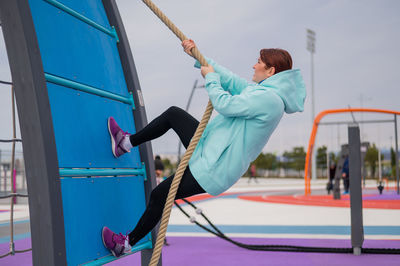 Low angle view of woman rope climbing at public park