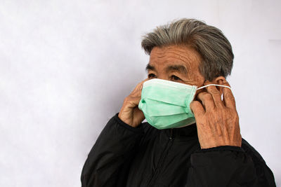 Senior woman putting on mask against white wall