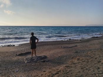 Rear view of man standing on beach against sky