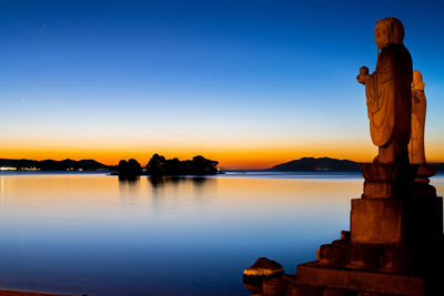 Statue by lake against clear sky during sunset