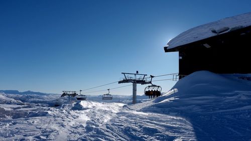 Low angle view of ski lift over snowy field against clear sky on sunny day