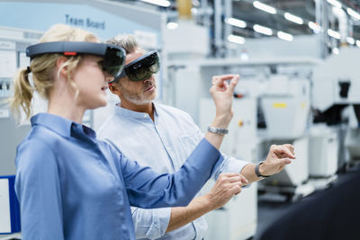 Coworkers discussing and using augmented reality eyeglasses in factory