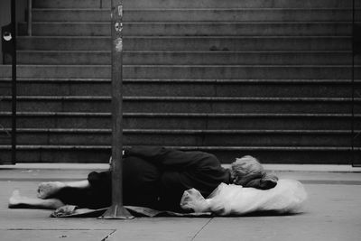 Man sleeping on footpath against wall