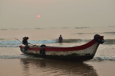 Fishing boat and woman in sea against sky during sunset