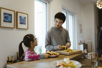 Brother peeling banana while standing near sister in kitchen at home