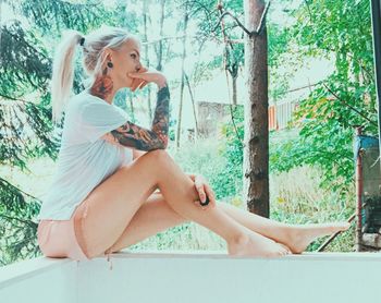 Side view of thoughtful young woman sitting on railing against trees