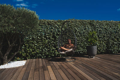 Man sitting on seat against hedge