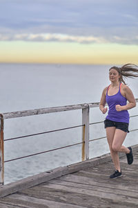 Woman jogging on pier over sea against sky
