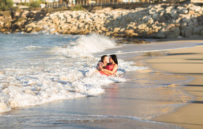 Full length of couple embracing while sitting on beach