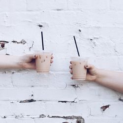 Cropped hands holding cold coffee against wall