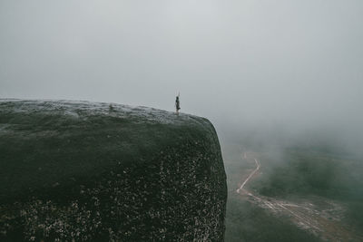 Woman standing on cliff during foggy weather against sky