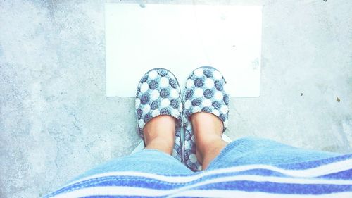 Low section of woman wearing slippers while standing on tiled floor