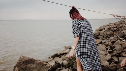 Rear view of woman standing on rock by sea against sky