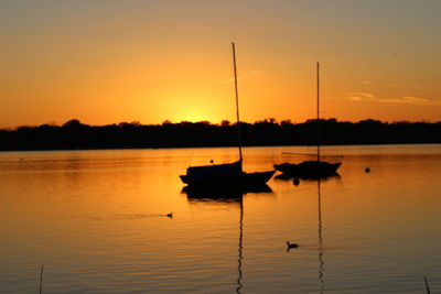 Silhouette boat in lake against orange sky