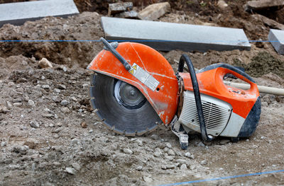 A worn, bright orange petrol saw with diamond cut-off wheel set against blurred background of rubble