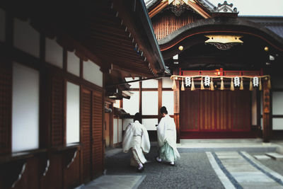 Rear view of people in traditional clothing walking by temple