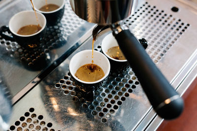 From above freshly aromatic coffee in compartment at coffee machine with coffee mugs