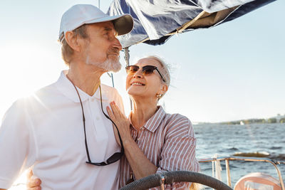 Smiling senior couple standing on boat in sea against sky