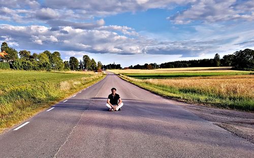 Man sitting on road against sky