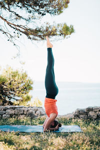 Side view of woman exercising against sky