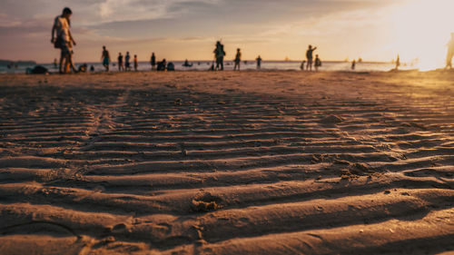 Surface level of people on beach against sky during sunset