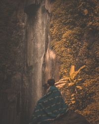 Man sitting on mountain against waterfall