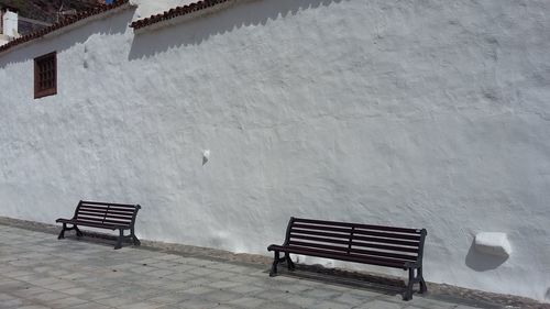 Empty benches on snow covered bench against building