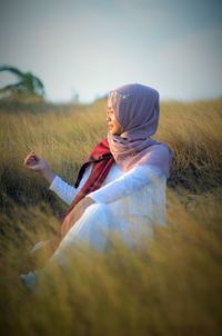 Woman wearing hijab sitting on grassy land