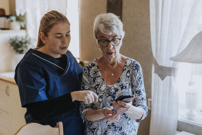 Home caretaker helping senior woman use smart phone