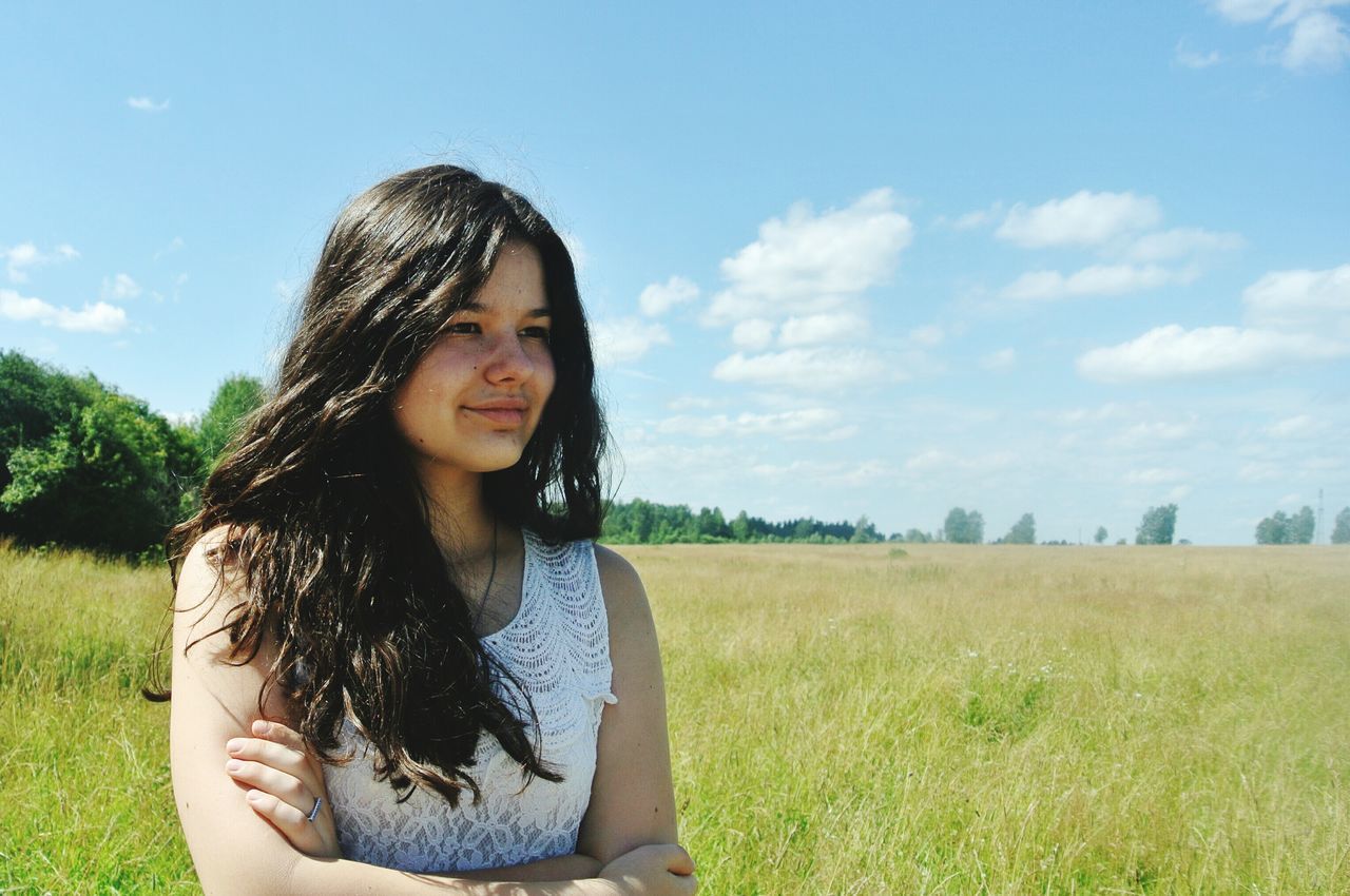 person, grass, young adult, lifestyles, portrait, smiling, leisure activity, looking at camera, young women, casual clothing, sky, field, front view, tree, grassy, happiness, long hair