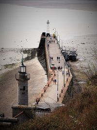 People walking on pier at beach with lighthouse