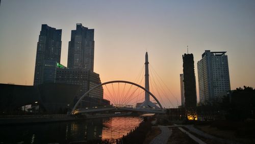 Bridge over river in city against sky during sunset