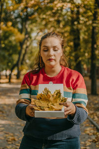 Beautiful woman holding autumn leaves standing at forest