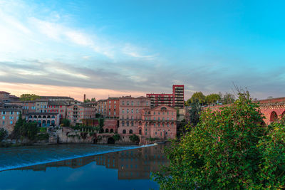 Buildings by swimming pool against sky during sunset